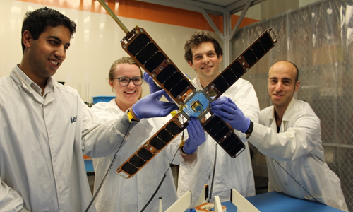 Group of four researchers wearing gloves and lab coats holding a microsatellite