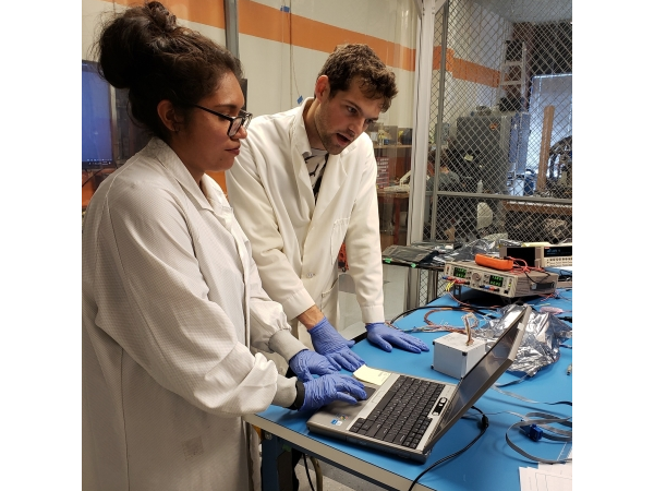 Two Students Wearing Lab Coats Typing on a Laptop