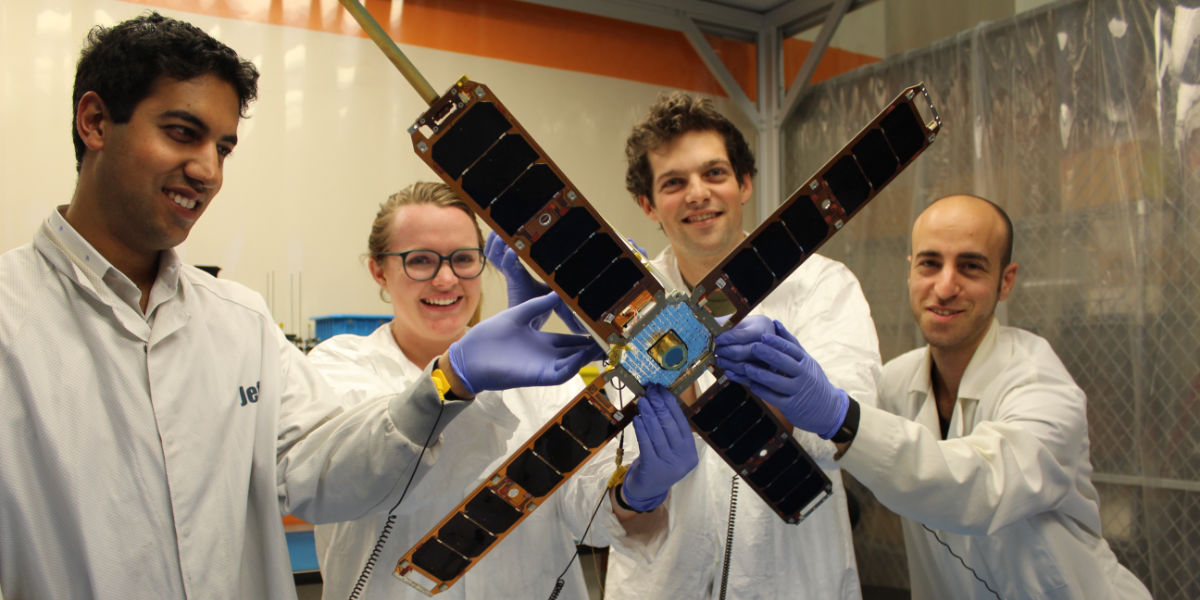 Group of four researchers wearing gloves and lab coats holding a microsatellite