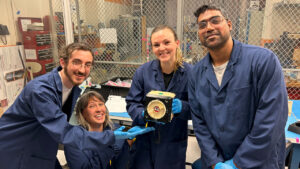 Group of researchers wearing lab coats and gloves holding cube microsatellite