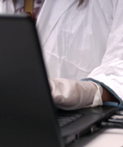 Researcher Typing on Computer Wearing Lab Coat and Gloves