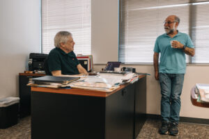 Person seated on office chair engaged in discussion with person standing across office desk