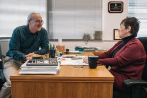 Person seated on office chair engaged in discussion with person seated across office desk